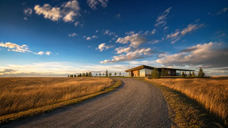 Open prairie road leading to a modern community hall with a flag pole and low trees under a wide sky, no text, no people, Doing Business in Indian Country in Oklahoma